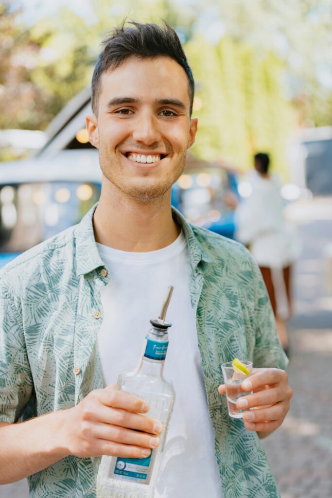 Cheerful young man outdoors holding a bottle of tequila and a shot glass with lime.